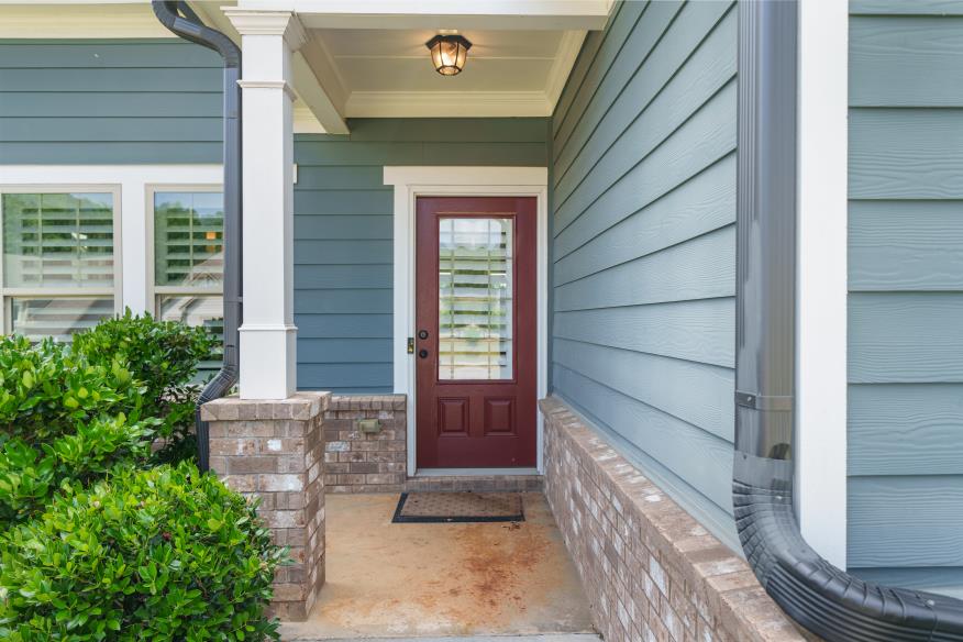Covered front porch entryway featuring a red door, brick accents, and light blue siding.