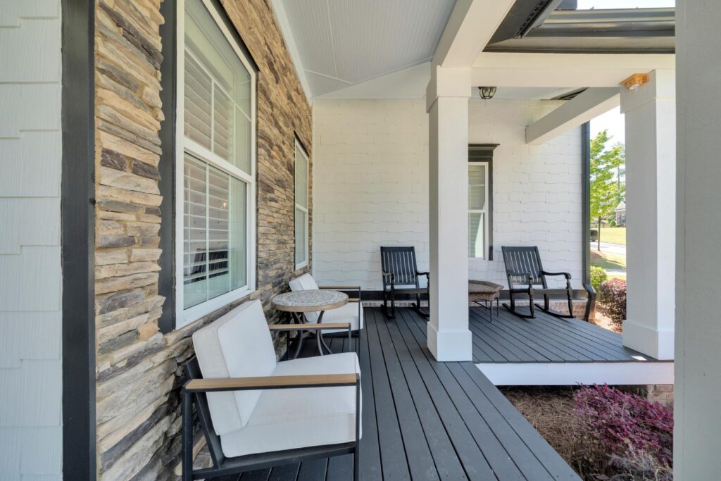 Covered front porch with cushioned chairs and stone accent wall creating a cozy outdoor seating area.