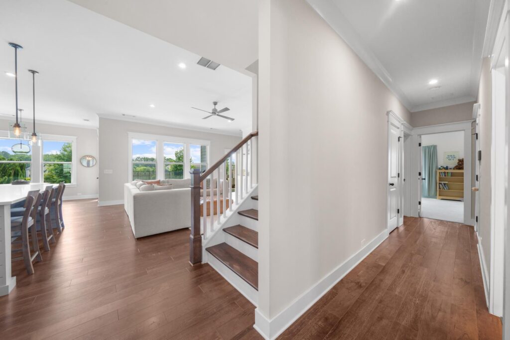 Open-concept hallway and living space with hardwood flooring, white walls, and natural light from large windows.