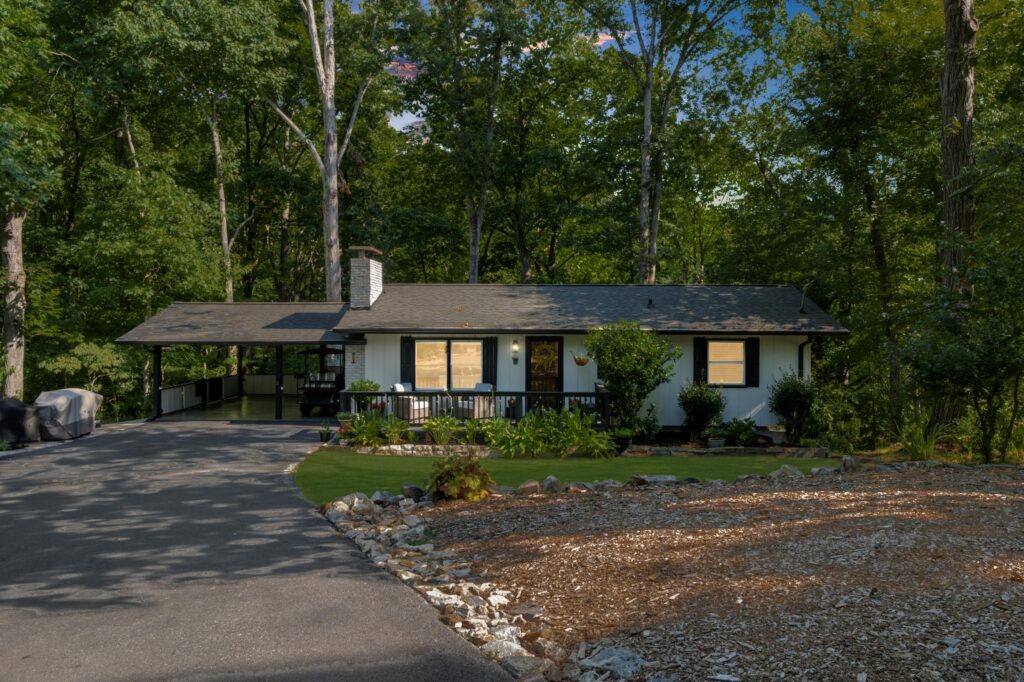Single-story home surrounded by trees, featuring a black front porch and garden.