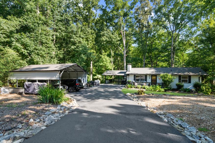 Long driveway leading to a forest-surrounded ranch house with detached covered parking.