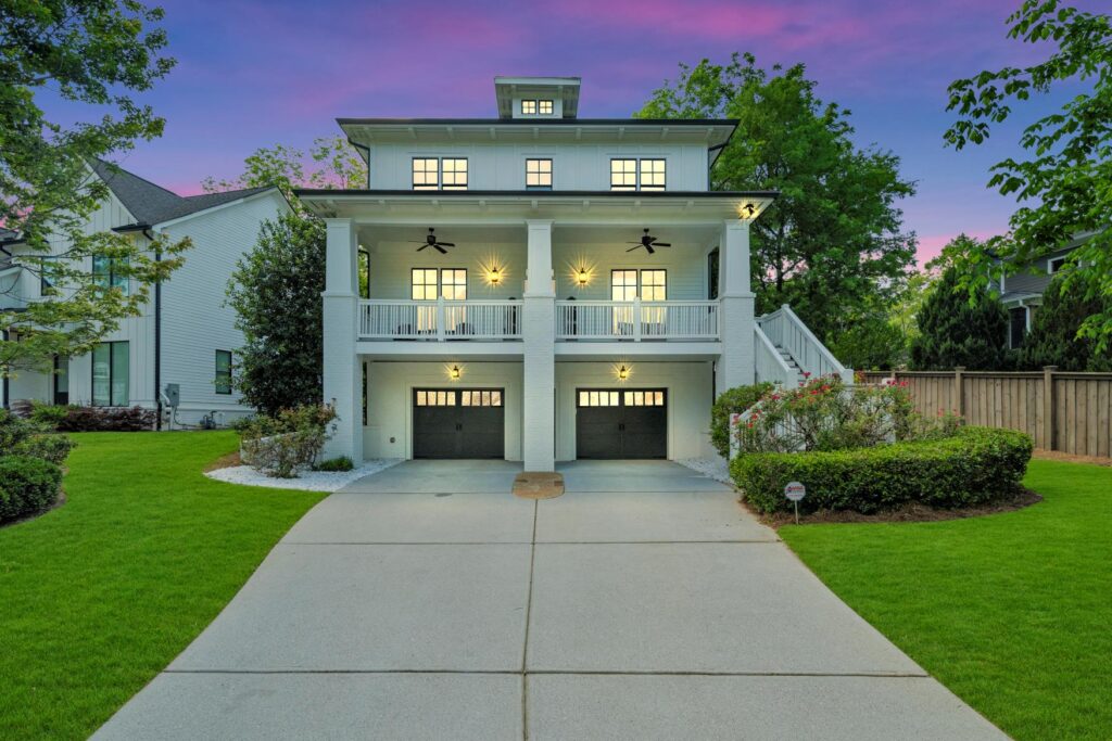 Three-story modern colonial-style house with double garage, large balconies, and evening lighting.